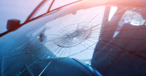 Close up of a windscreen that has been hit with an object resulting in many cracks extending out from the point of impact.