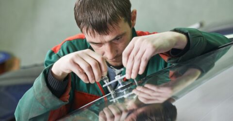 A man concentrating on the repair of process of a small crack in a windshield.