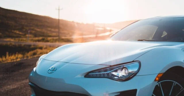 A car parked on an empty road under the sun.