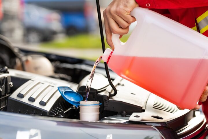 Service worker man pours red washer liquid in a car hood.