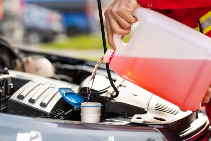 Service worker man pours red washer liquid in a car hood.