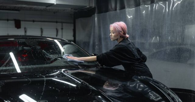 A woman washing and wiping a car windscreen.