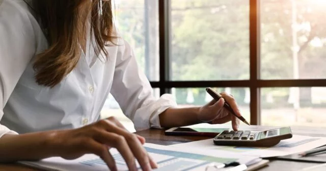 Woman doing some calculations with a calculator, computer and invoice.