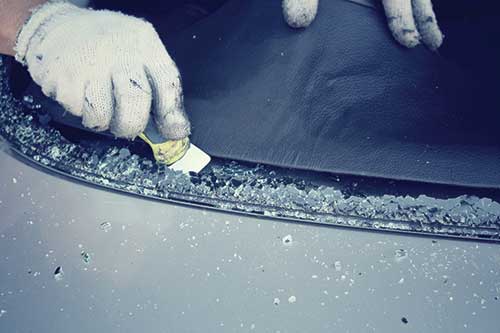 Broken glass being scraped out of a smashed windscreen