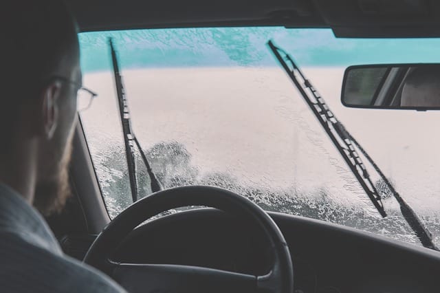 View from inside car looking out and seeing wipers clearing rain from windscreen