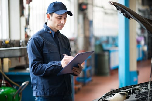 Mechanic with clip board running through check list in front of car.